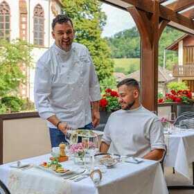 Herr Mannel serviert dem Gast auf der Terrasse eine Speise
